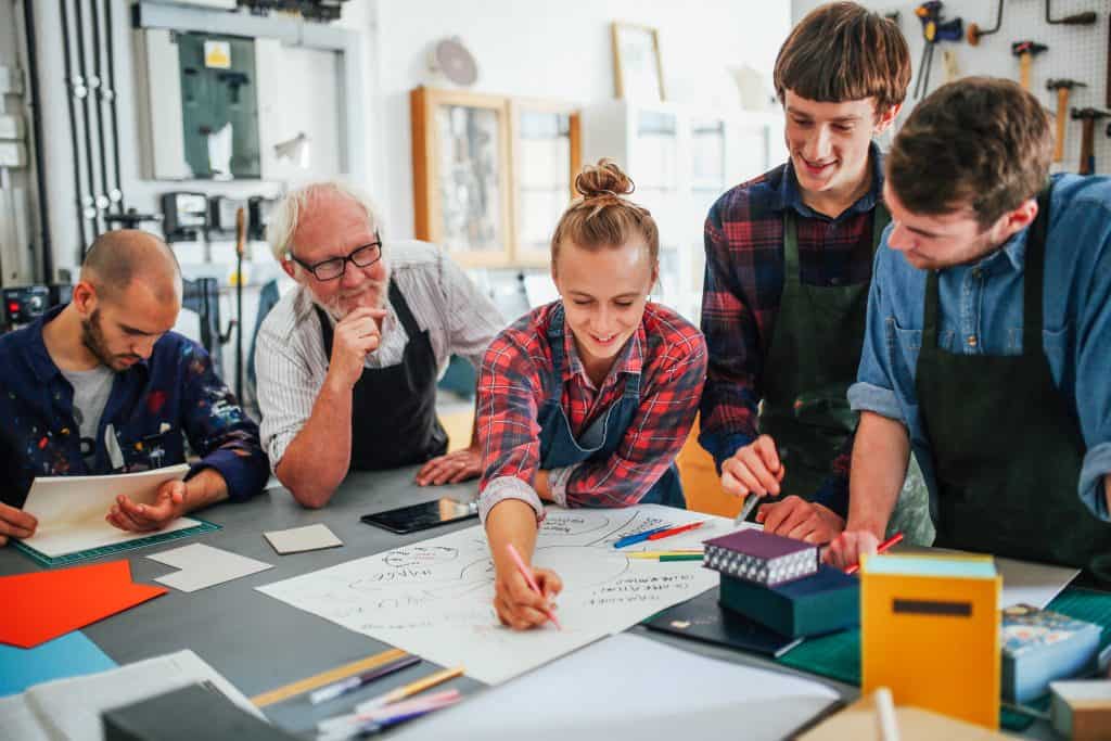 Senior male craftsman brainstorming ideas with group of young men and women in book arts workshop